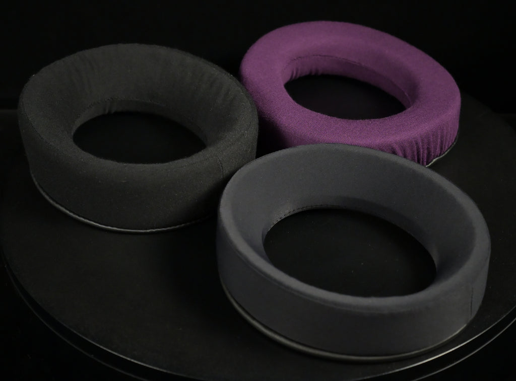 Three ETA ULI replacement earpads in black, purple and gray displayed on a black rotating stand
