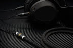 ETA headphone connected with Audiophile Ninja UPOCC dual 3.5mm cable, close up on carbon fiber surface