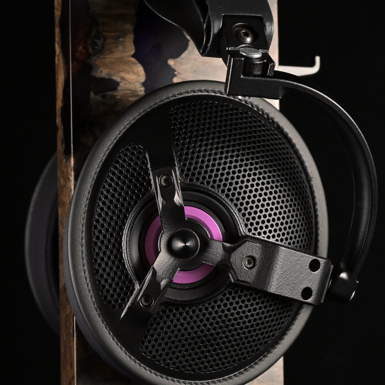 ETA ULI AlNiCo open-back headphone on a burl wood and resin display stand, close side view of the earcup showing the perforated grille, three-spoke driver chassis and purple voice coil